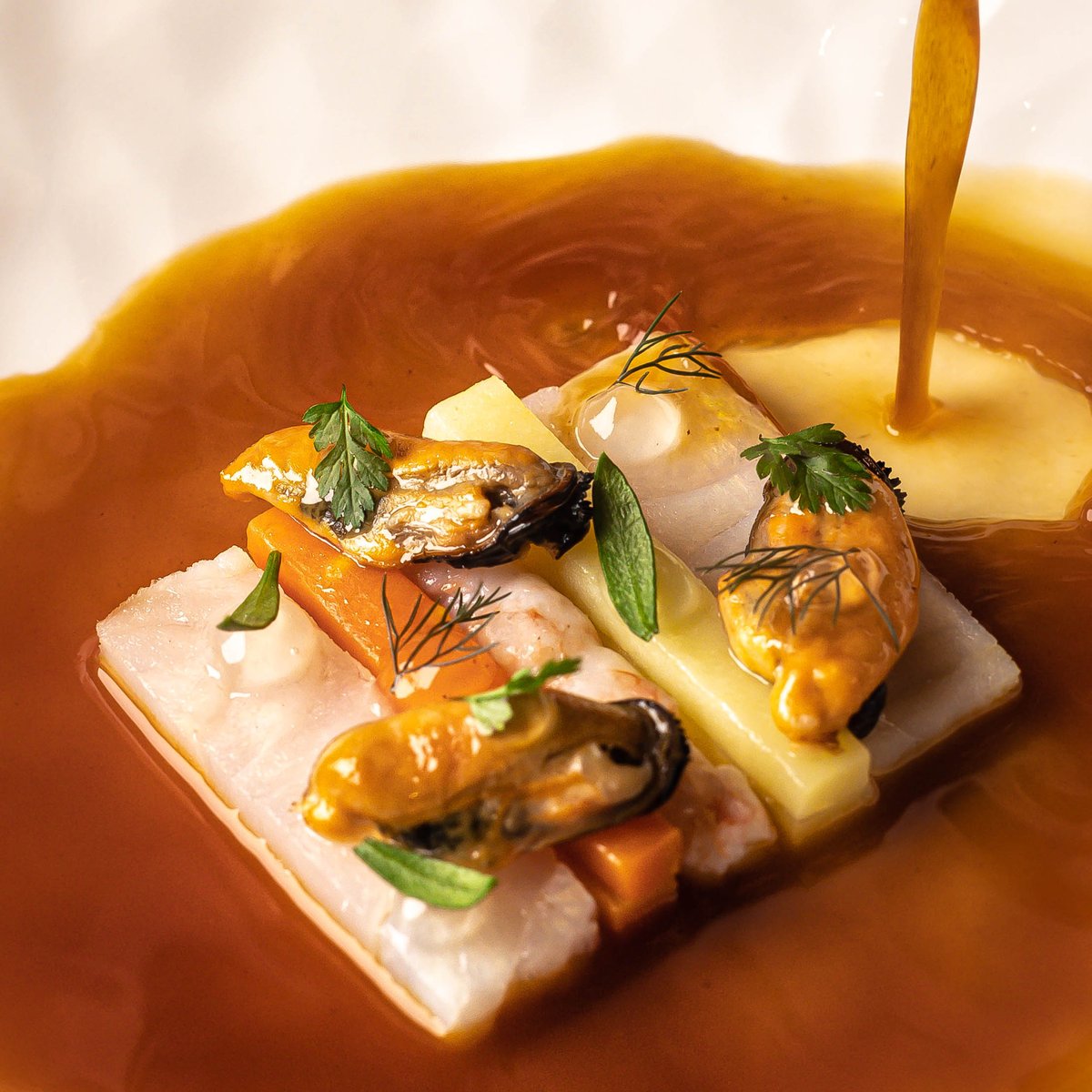 Un poisson servi dans son bouillon ambré, coquillages et herbes — la cuisine de Contraste